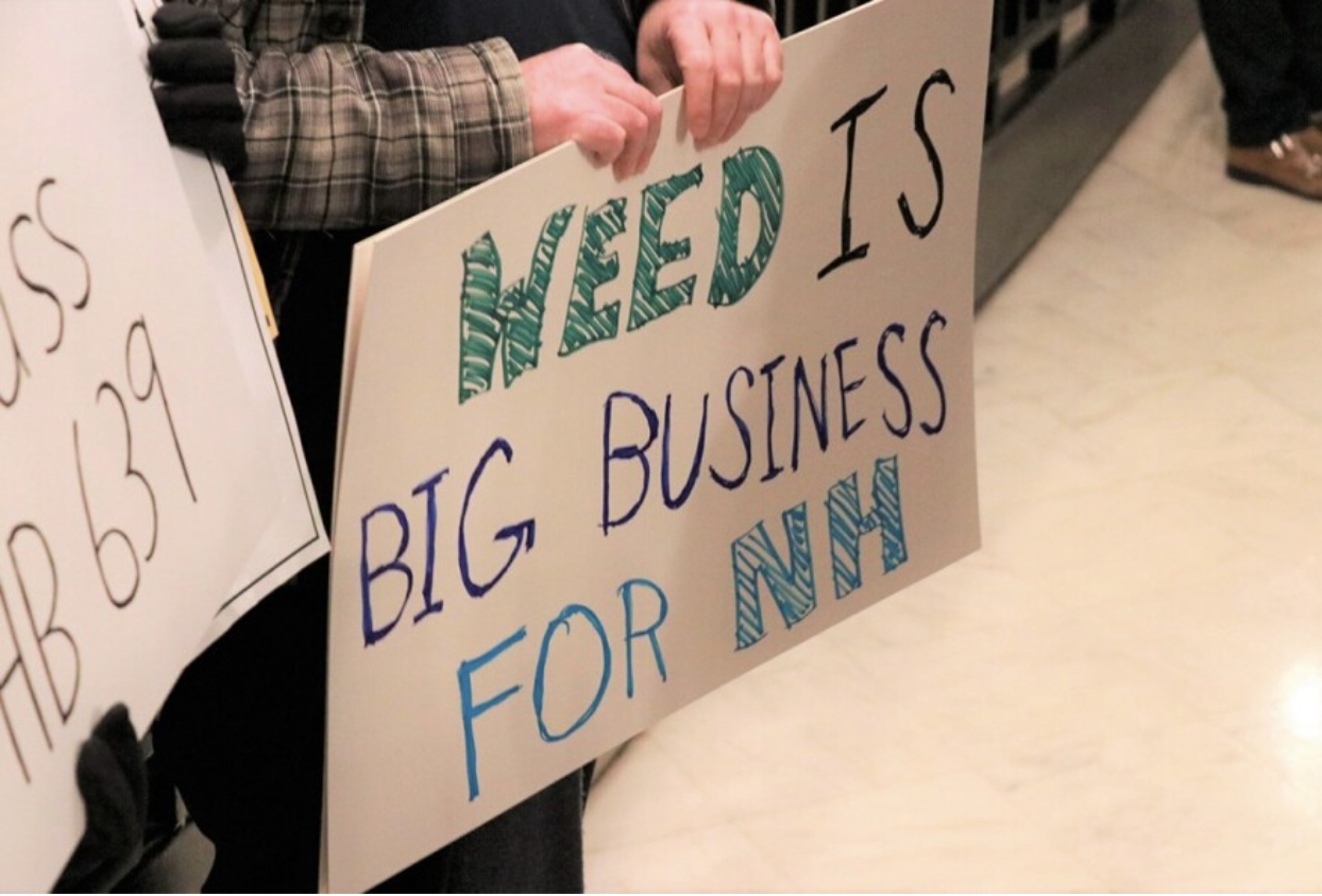 A person holds a sign supporting marijuana legalization as state representatives enter the New Hampshire House of Representatives on April 6, 2023.