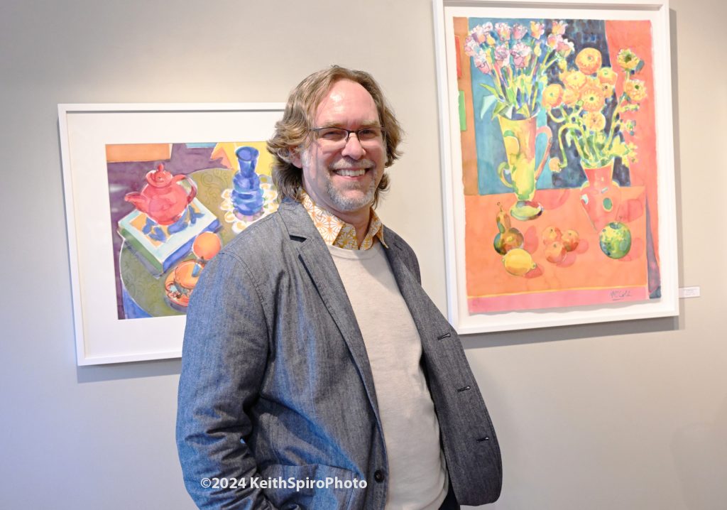 Artist Bruce McColl standing between two of his watercolors on display at Sullivan Fine Art Gallery. A photograph by Keith Spiro